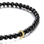 Black beaded bracelet with a gold ring on a white background