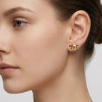 Close-up of a woman wearing gold Koala shaped earrings with red enamel flower on a neutral background