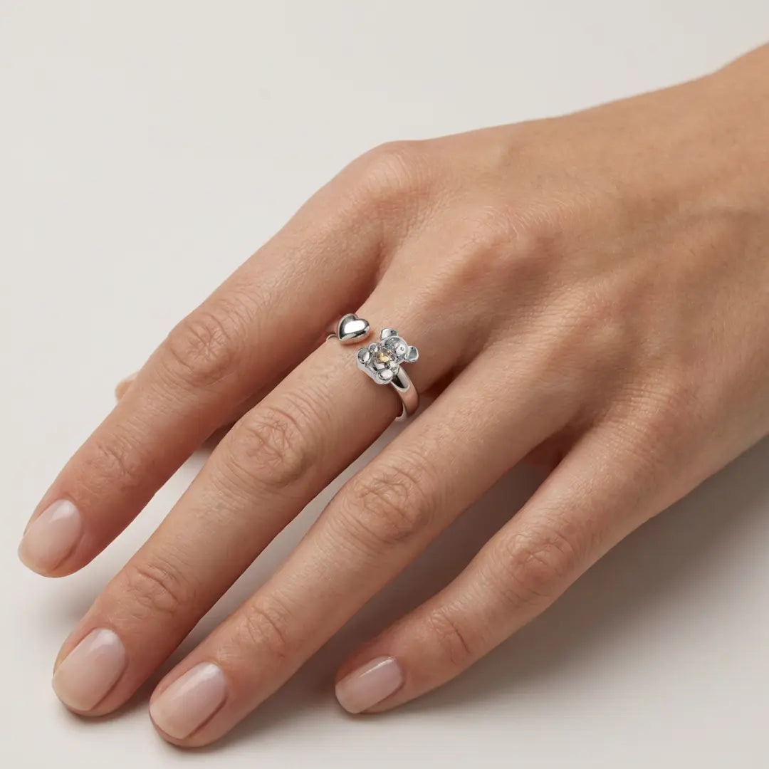 Hand model wearing a silver ring with a small Koala & 10k Gold Heart on a light background